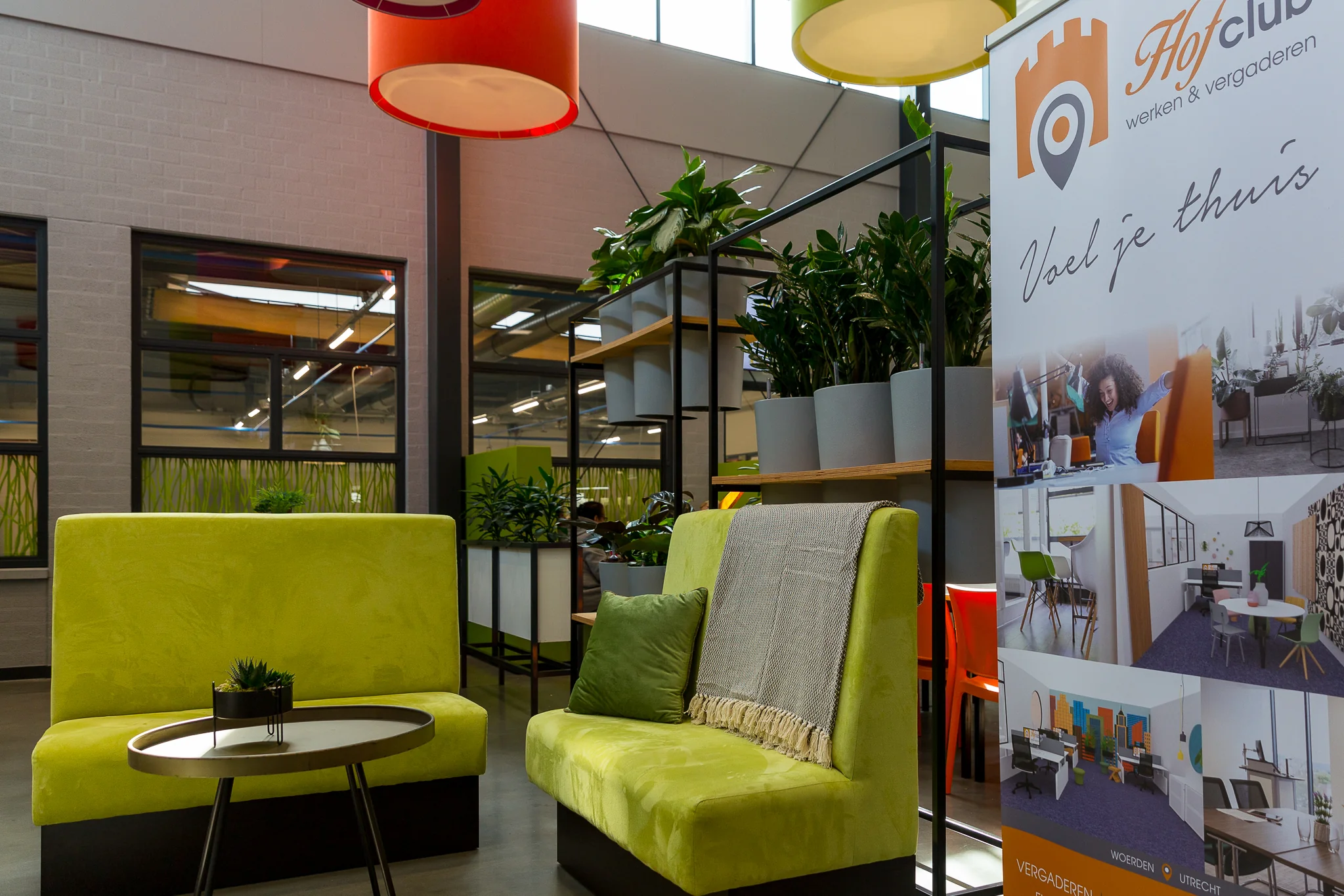 Moderne wachtruimte of loungehoek met groene zitbanken, planten en een banner van Hofclub werken & vergaderen.